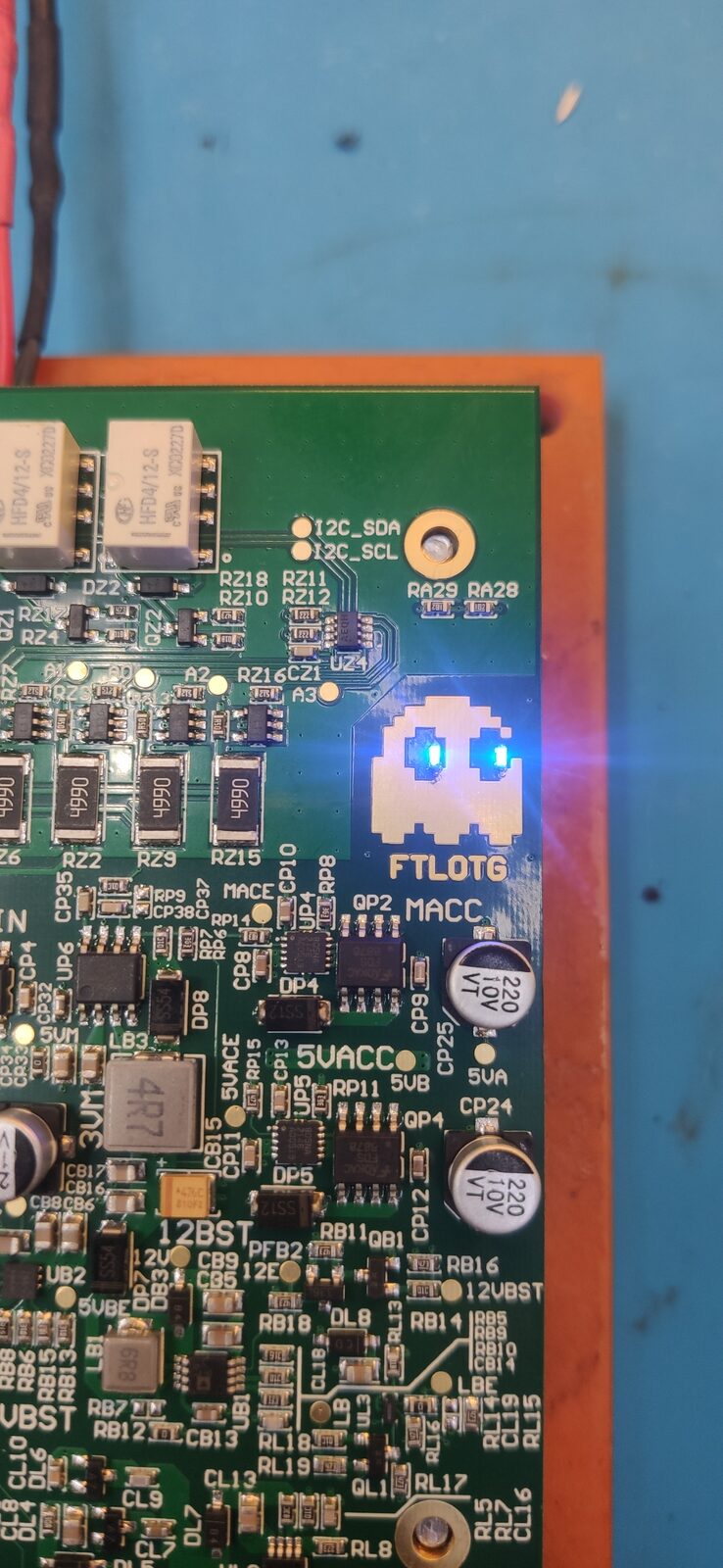 Dark circuit board with many small components and a glowing blue ghost-shaped light, lit on an orange base over a blue mat.